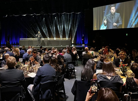 crowded open-spaced room with man on stage accepting an award and giving a speech