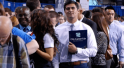 Photo of crowd of business professional-dressed people at career fair, man in middle holds a folder that reads City Career Fair.