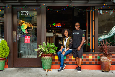 Two individuals standing outside Island Soul Restaurant entrance with colorful tilework and potted plants.