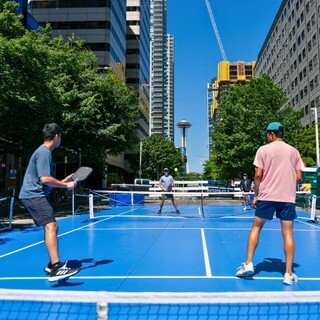 Four people playing pickleball outside with the Space Needle in the background.