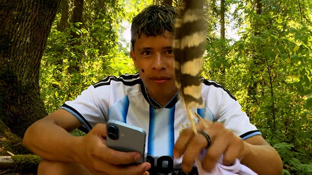 A student holds a bird feather in the forest. 