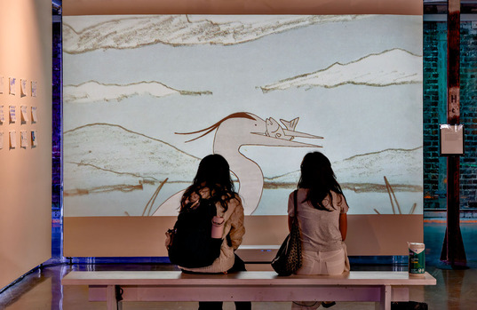 Two people watch an animation of a heron with a fish in its beak.