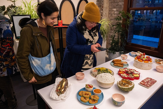 Realistic Vietnamese food made out of ceramics. Two people look down at it, one takes a photo.