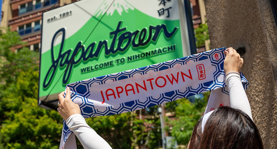 A person holding a Japantown scarf underneath a Japantown sign