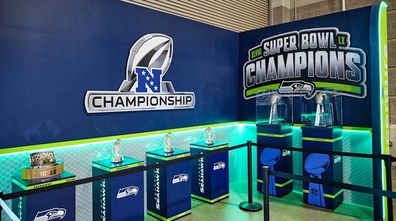 Seattle Seahawks championship trophy display featuring NFC and 2026 Super Bowl trophies on branded podiums behind a barrier.