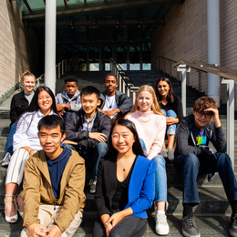 Group portrait of 10 young people seated on the steps outside a building entrance.