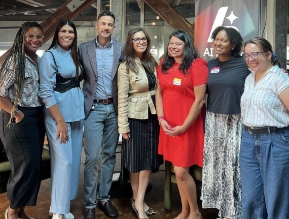 Group photo of seven smiling people, including Beto Yarce, standing indoors at a professional AI-related event.