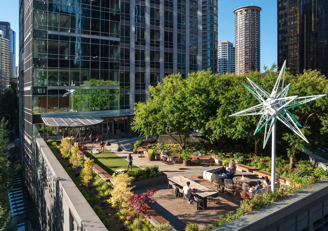 A rooftop garden atop a downtown building with trees, people, and tables.