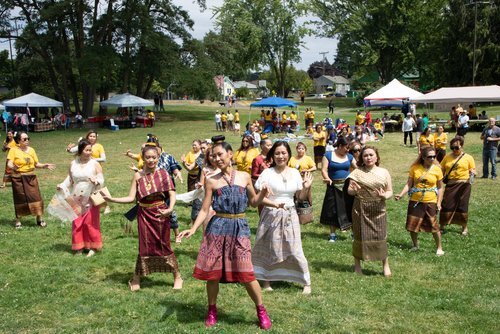 A large group of Lao women, some in traditional dress, dance on the grass in the park.