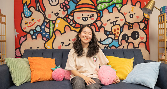 Kira, owner of ichigo alley, sitting on a couch holding plushies