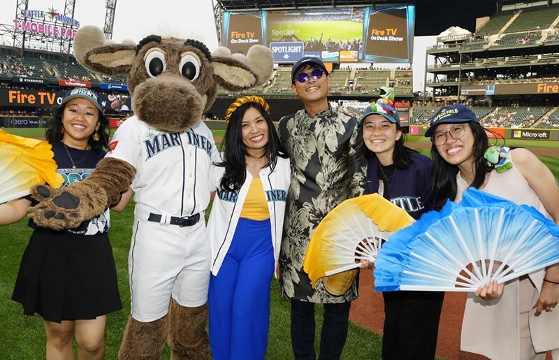 A group of smiling fans wearing Mariners gear pose with a mascot at Vietnamese Heritage Night.