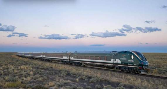 Photo of an Amtrack train moving through plains across a setting sky.