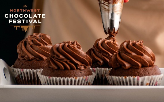 A piping bag adds chocolate frosting to one of four chocolate cupcakes on a white tray, with "The Northwest Chocolate Festival" logo in upper left.