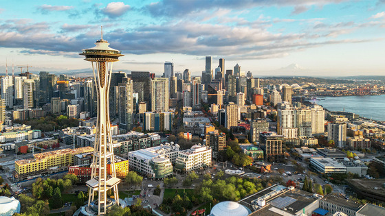 Aerial view of Seattle at golden hour: the Space Needle stands left, downtown towers fill the center, and Mount Rainier rises beyond Elliott Bay.