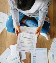Top view shot of person looking down at multiple bills laid out around them.