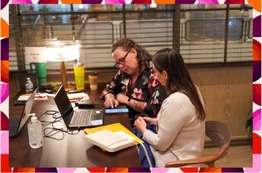 Two women seated together looking other items on a phone. Colorful purple, pink, and orange abstract blob border.