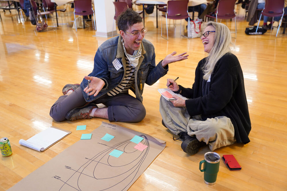 Two people laugh while seated on the floor.