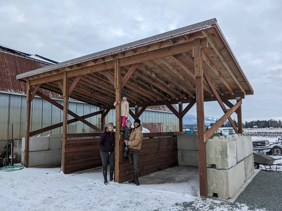 The Van Loo family standing in the snow in front of a large structure with a wooden cover, concrete floor and ecology block walls.