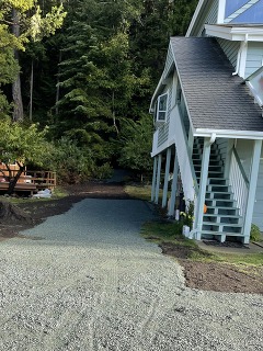 A strip of fresh gravel runs alongside a light blue house. This is the site where an underground pipe was recently replaced.
