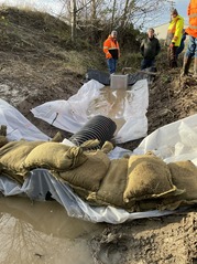 Pooled water in a ditch stopped by sandbags and plastic sheeting. A pipe allows the cleaner, settled water to pass through the dam.