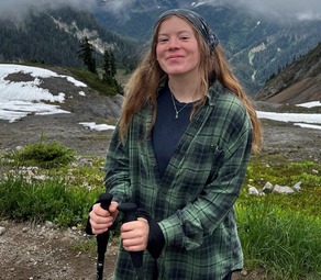 A young person with a bandana and hiking poles standing in mountains with fog and patches of snow.