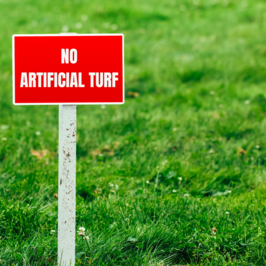 A red sign that reads "No artificial turf" on a lawn.