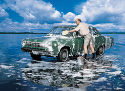 A man washing a car with soap. The car is parked in the middle of an ocean mudflat.