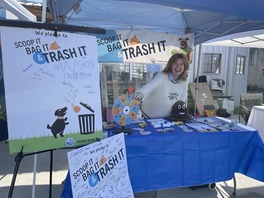 Girl spinning a trivia wheel from behind an educational booth with posters saying "Scoop it, bag it, trash it!"