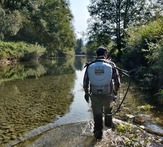 Person with herbicide backpack wading through a creek.