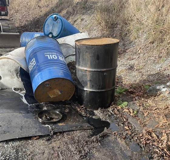 Several 55-gallon barrels on a roadside with material leaking out of them.