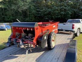 Red manure spreader sitting on the back of a trailer.