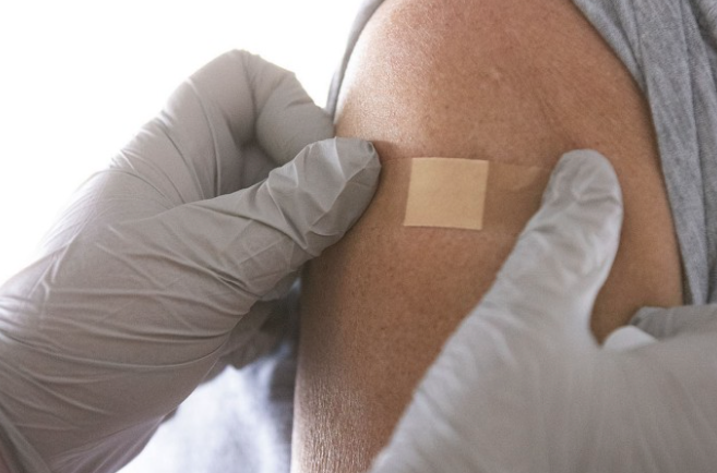 Gloved hands placing bandaid on upper arm of person
