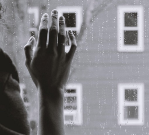 Person looking outside with hand against rainy window