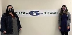 Emily Oomen and Heather Thomas with Snohomish Health District stand in front of a 6 feet apart sign