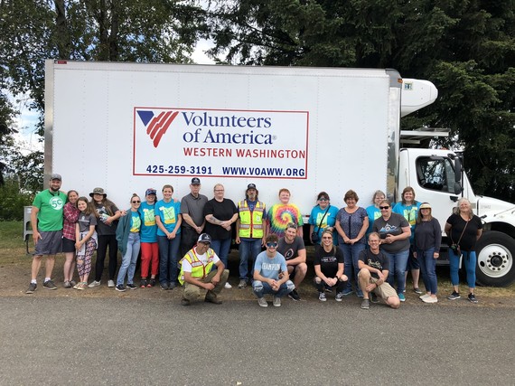 Volunteer stand smiling in front of a Volunteers of America truck.
