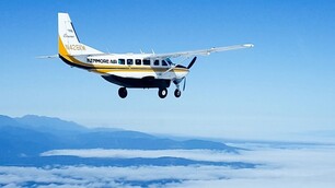 A yellow and white Kenmore Air Cessna Caravan above the clouds