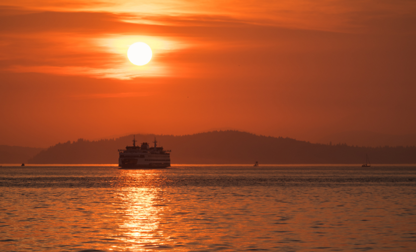 A photo of a Washington State Ferry crossing Puget Sound while the air is full of wildfire smoke, giving the whole picture and orange smoky cast.