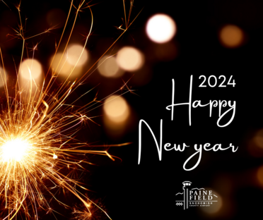 A gold sparkler glows next to words "2024 Happy New Year" with the Paine Field official logo