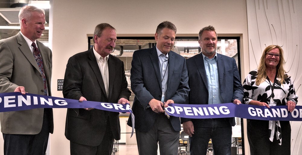 A group of elected officials and community partners stand behind a purple ribbon that says "grand opening."
