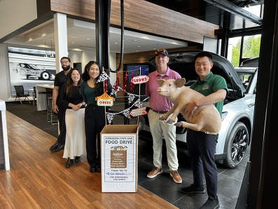 Lee Johnson Auto Family Employees holding a fake pig infront of food drive box. 