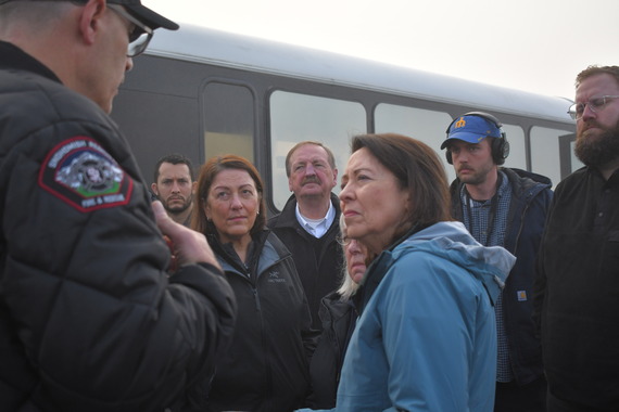Executive Somers and other elected leaders stand in a group listening to a first responder speak