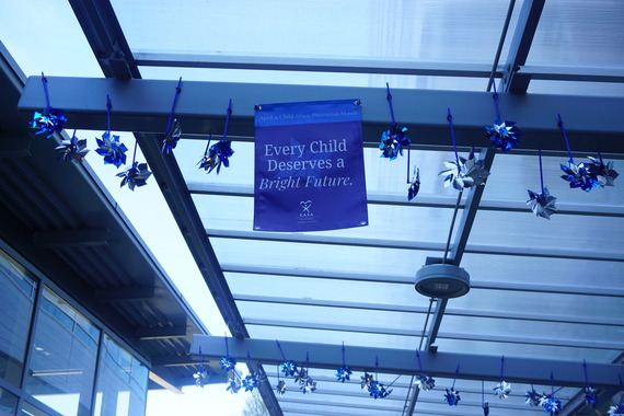 Pinwheels hang from an outdoor covered walkway with a sign that says "Every Child Deserves a Bright Future"