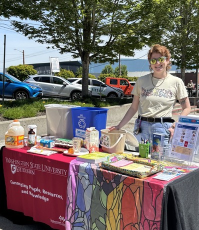 WSU vendor standing behind a resource table with a Pride flag to resemble stained glass at the Pride Resource Fair