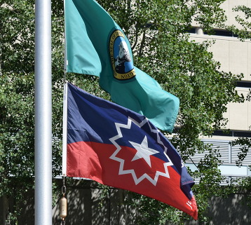 Green Washinton State flag with President George Washington on it. The Juneteenth Flag with red, blue and white. 