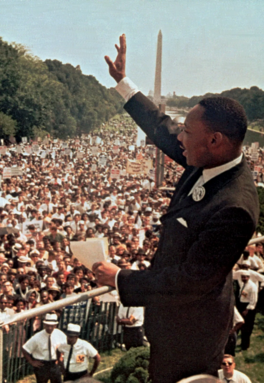 Dr. Martin Luther King, Jr. raising his hand to wave to a crowd of people at the Reflection Pool in Washington, D.C.