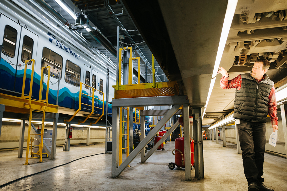Photo of a worker standing next to a link light rail car on a riser at a Link Maintenance Facility