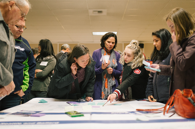 Photo of people standing around a table viewing documents, Everett Link Extension