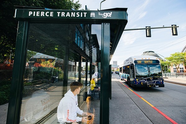 Photo of a rider at a Piece Transit bus stop with a Sound Transit bus approaching