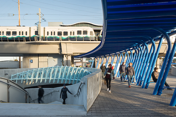 Image of people walking around Angle Lake Station with the link light rail passing by. 