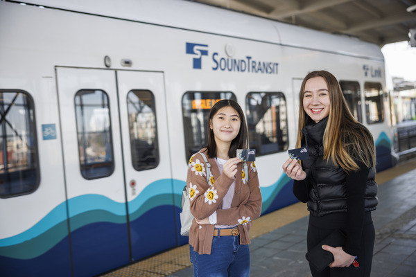 Two youths holding ORCA cards stand in front of a Link light rail.